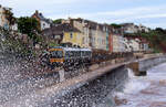 Regionalzug fährt hinter hohen Wellen Richtung Exmouth. Dawlish, 17.5.2022