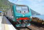 Trenitalia E464.664, Bj. 2012, mit Regionalzug R 24496 La Spezia C.le – Sestri Levante hlt in Bf. Corniglia [Cinque Terre], rechts im Hintergrung Ort Manarola; 09.05.2013 