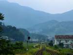 Matsuura-Bahn: Blick in den blauen Dunst der hohen Berge an der Bucht von Imari. In der Ferne nähert sich der Einzeltriebwagen 401. Kusuku, 26.Juli 2013. 