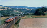 Im Juli 1991 ist 1042 020-5 mit einem Regionalzug auf der alten Westbahnstrecke bei Säusenstein unterwegs, dahinter die Donau und auf der Anhöhre rechts die Wallfahrtskirche Maria Taferl