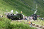 Die Lok HG 4/4 704 wird mittels Muskelkraft auf der Drehscheibe abgedreht. Do - Sa findet in der Station Furka jeweils am Nachmittag die Kreuzung mit dem roten Zug (Oberwald - Realp) und dem blauen Zug (Realp - Oberwald) statt. Die HG 4/4 muss hier immer abgedreht werden, weil wegen der Bauart der Lok das Kamin sich immer bergwärts befinden muss (die Station Furka ist mit 2160 müM die höchste Station der Strecke). Weil das Gleis für die Fahrt der Lok von der Zugspitze zur Drehscheibe durch den blauen Zug belegt ist, muss jeweils aufwändig rangiert werden: Nach der Einfahrt des roten Zuges ins Gleis 1 wird dieser zurück geschoben. Dann wird die Lok abgekuppelt, fährt auf die Drehscheibe, wird dort gewendet und fährt wieder an die Wagen an. Nach dem Ankoppeln fährt der Zug dann wieder ins Gleis 1 ein. Furka, 20.7.2024