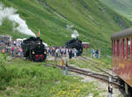 Die Lok HG 4/4 704 wurde auf der Drehscheibe abgedreht und fährt wieder an die roten Wagen an. Do - Sa findet in der Station Furka jeweils am Nachmittag die Kreuzung mit dem roten Zug (Oberwald - Realp) und dem blauen Zug (Realp - Oberwald) statt. Die HG 4/4 muss hier immer abgedreht werden, weil wegen der Bauart der Lok das Kamin sich immer bergwärts befinden muss (die Station Furka ist mit 2160 müM die höchste Station der Strecke). Weil das Gleis für die Fahrt der Lok von der Zugspitze zur Drehscheibe durch den blauen Zug belegt ist, muss jeweils aufwändig rangiert werden: Nach der Einfahrt des roten Zuges ins Gleis 1 wird dieser zurück geschoben. Dann wird die Lok abgekuppelt, fährt auf die Drehscheibe, wird dort gewendet und fährt wieder an die Wagen an. Nach dem Ankoppeln fährt der Zug dann wieder ins Gleis 1 ein. Furka, 20.7.2024