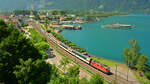 Ein Kommen und Gehen in Flüelen: Der Blick vom Kirchberg auf den Ort und den Vierwaldstättersee. Die Re 4/4 11199 beschleunigt den Gotthard Panorama Express (GoPEx) aus dem Bahnhof und wird in Kürze sein Ziel Arth-Goldau erreichen. Kurz darauf läuft das Dampfschiff  URI  in den Hafen ein und nimmt nicht nur die Fahrgäste des Zuges auf. (19. Juni 2022)