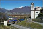 Die Kirchuhr der schönen Kirche San Carlo von Magadino zeigt kurz vor eins, als eine SBB Re 474 mit ihrem Güterzug durch den ruhigen Feiertag (San Giuseppe) Richtung Luino fährt.