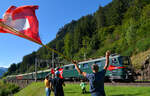 Gotthard-Bahntage: Auf der Talfahrt von Göschenen nach Erstfeld kommt Ae 6/6 11411 pfeifend an Xaver Andermatt und seinem Fahnenspalier vorbei.