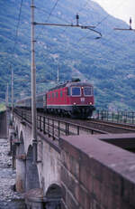 Auf der Simplon-Eisenbahn gelangen Schweizer Lokomotiven bis ins italienische Domodossola - erst dort stößt das 15kV 16,7 Hz System auf die 3 kV Gleichstrom der FS. Hier überquert die Re 6/6 11636 der SBB mit einem internationalen Schnellzug den Fluß Bogna kurz vor dem Bahnhof Domodossola.
Domodossola, 28. Juni 1988; Canon AE-1, Canoscan, Gimp