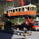 BLM Bergbahn Lauterbrunnen-Mürren: CFe 2/4 11 (SIG/MFO 1913), Verlad auf den Strassentransporter zur Fahrt nach Rain (Aussendepot des Verkehrshauses in Luzern), Lauterbrunnen, 24. Oktober 2024. Die beiden Autokrane haben den Triebwagen vom Geländetransporter  Castor und Pollux  angehoben, dieser ist weggefahren, der Lastwagen manöveriert unter die schwebende Last.