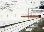 Matterhorn-Gotthard-Bahn__Zug von Andermatt fährt in die Station Oberalppass (2033m) ein. Im Hintergrund Gondeln der Schneehüenerstock-Kabinenbahn.__25-02-2024