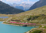 Der Regionalzug von Tirano nach St. Moritz fährt mit den beiden offenen Aussichtswagen am Schluss in der Nähe des Bahnhofs Ospizio Bernina dem Lago Bianco entlang nordwärts. Zwischen dem Lago Bianco und dem Lej Nair im Hintergrund befindet sich die Wasserscheide Adriatisches- bzw Schwarzes Meer. Das Foto wurde vom Parkplatz bei der Bernina-Passhöhe aufgenommen. Ospizio Bernina, 21.8.2023